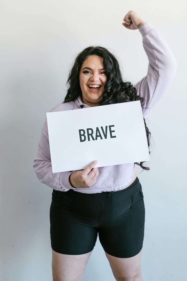 Enrich your spiritual life by being brave: A woman is holding a brave sign