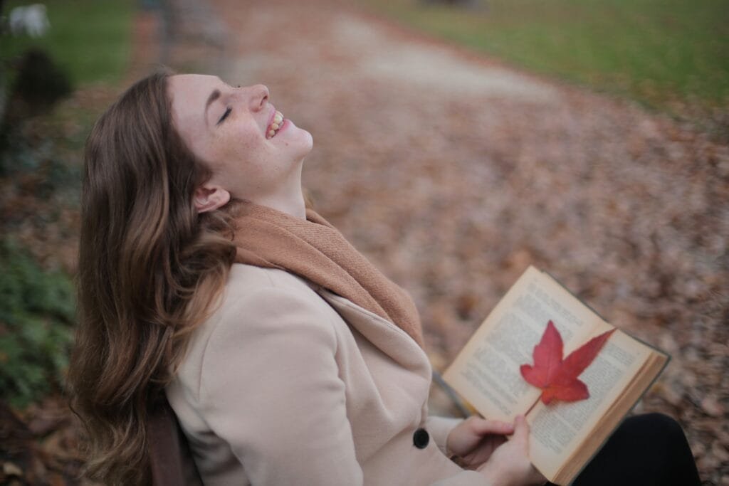 Smiling woman with an open book and leaf, reflecting a positive mindset and joy in nature.