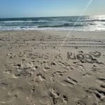 Footprints in the sand lead toward the ocean with the words “Jesus is King” written near the shoreline, under a bright sun—symbolizing trusting God for balance in a busy life.