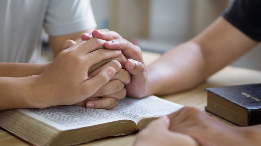Hands joined in prayer over an open Bible, reflecting guidance on how to start reading the Bible.